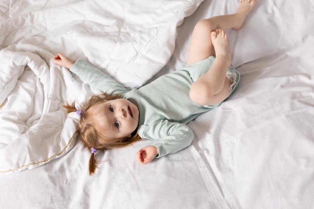 una niña pequeña con un traje verde claro está acostada en la cama hecha con ropa de cama blanca Foto de alta calidad