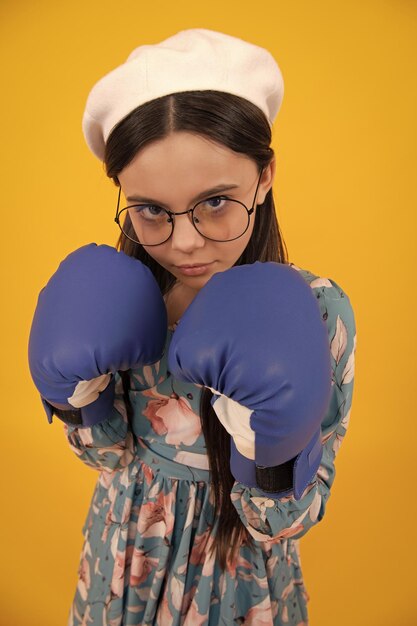 Niña pequeña usando guantes de boxeo con cara divertida Retrato de una adolescente ganadora sorprendida divertida en guantes de boxeo aislados en amarillo