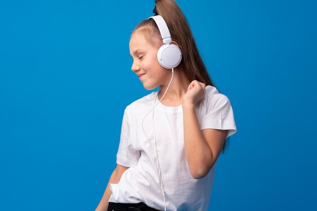 Niña pequeña use auriculares para escuchar música sobre fondo azul.