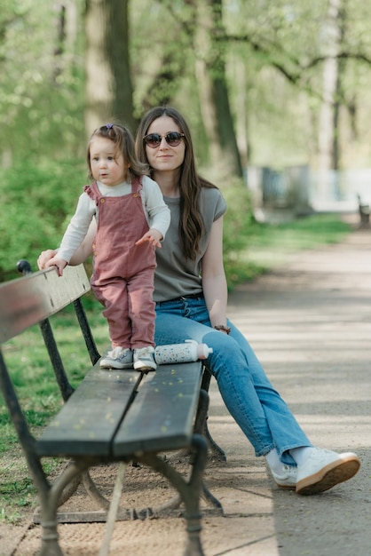 Una niña pequeña vestida de terciopelo está sentada en el banco con su madre.