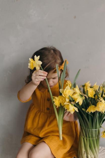 Niña pequeña con un vestido amarillo con un hermoso lazo sostiene una flor de narciso