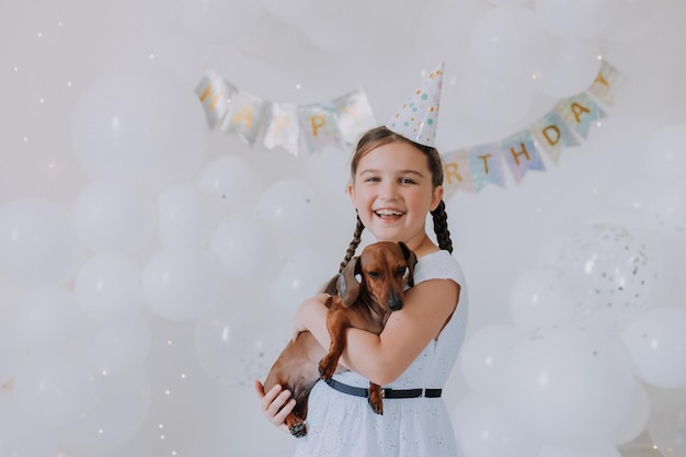 Niña pequeña con un vestido blanco con su amado perro salchicha en los brazos celebra su cumpleaños