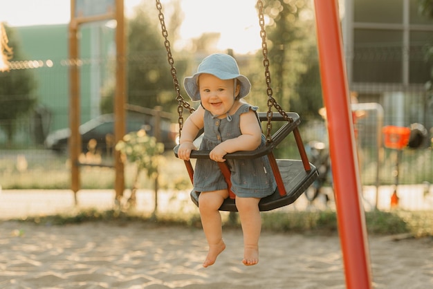 La niña pequeña con un vestido está feliz en un columpio en la cálida noche de verano