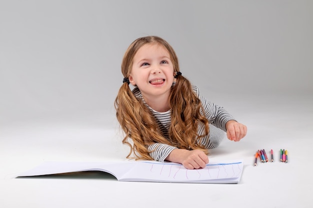 Niña pequeña con un vestido a rayas dibuja en un álbum tirado en el suelo estilo de vida de desarrollo infantil