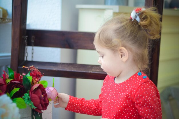 Niña pequeña con vestido rojo jugando en la habitación con adornos navideños