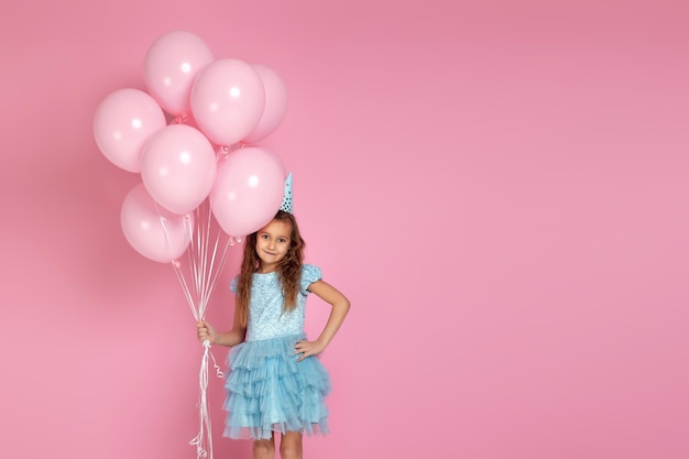 Niña pequeña con vestido y sombrero de cumpleaños celebrando con globos de aire rosa pastel