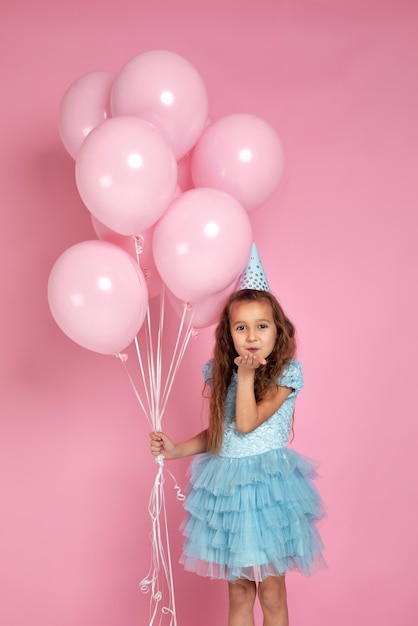 Niña pequeña con vestido y sombrero de cumpleaños con globos de aire rosa pastel