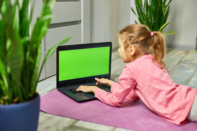 Niña pequeña viendo videos en línea en una computadora portátil y haciendo ejercicios de estiramiento en casa