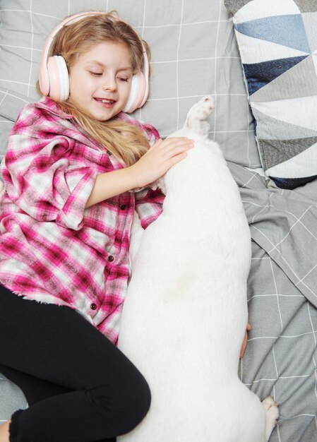 Niña y perro acostados en el sofá con auriculares, escuchando música con su teléfono inteligente.