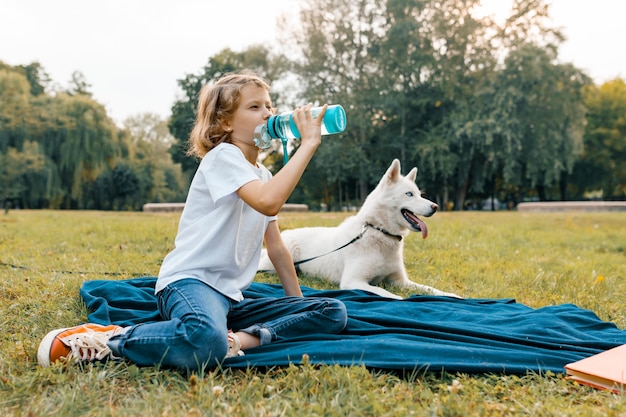 Niña con perro blanco en el parque sentado en el césped