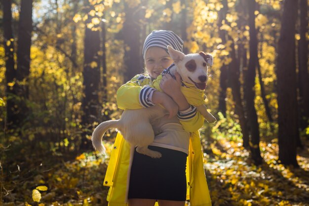 Niña con un perro jack russell terrier en el parque de otoño