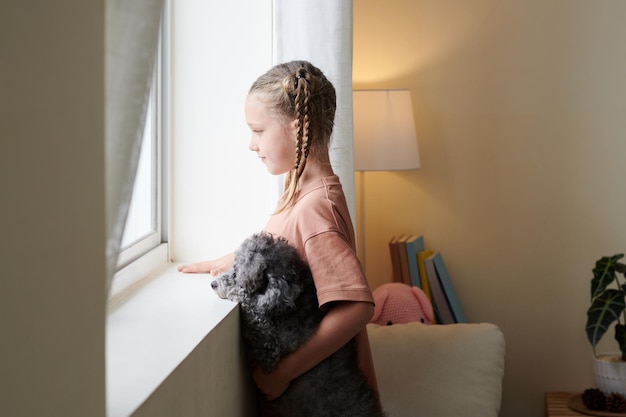 Niña y perro mirando por la ventana