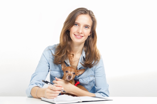 La niña con un perro pequeño sentado en una mesa y escribiendo notas en un cuaderno