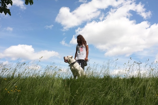 Foto niña con perro de pie en el campo de hierba contra el cielo
