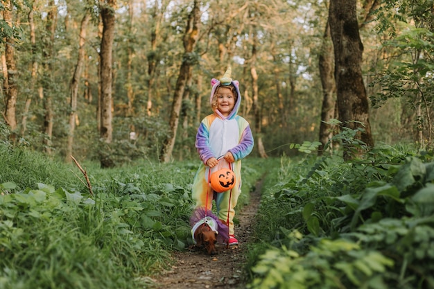 Niña y un perro salchicha enano en disfraces de Halloween están caminando en el bosque