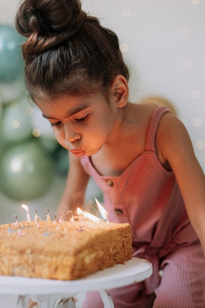 niña pide un deseo y sopla las velas del pastel de cumpleaños Niña linda celebrando su cumpleaños