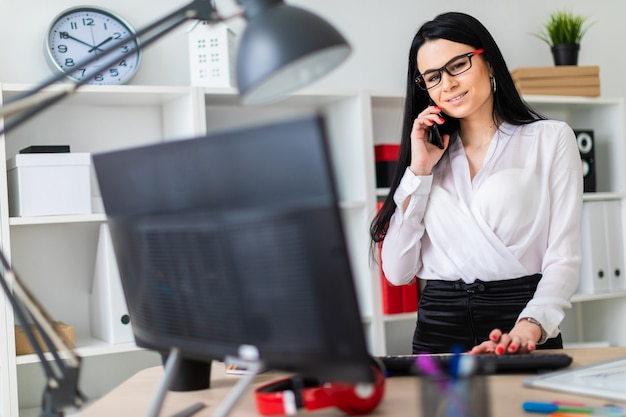 Foto una niña está de pie cerca de la mesa, hablando por teléfono y escribiendo en el teclado.