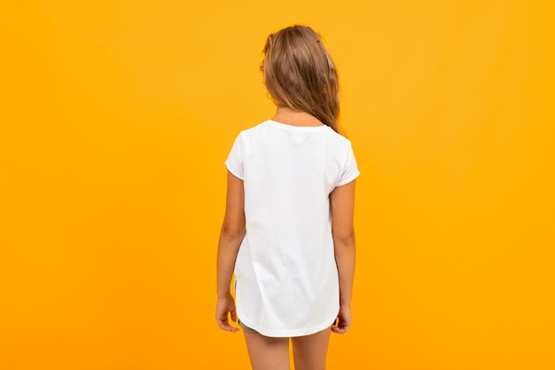 Niña de pie con la espalda en una camiseta blanca en una pared amarilla