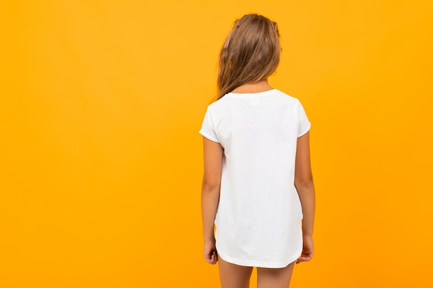 Niña de pie con la espalda en una camiseta blanca en una pared naranja