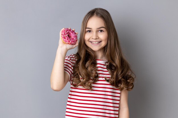 Niña de pie sosteniendo donut y sonriendo a la cámara mostrando dulces dulces azucarados