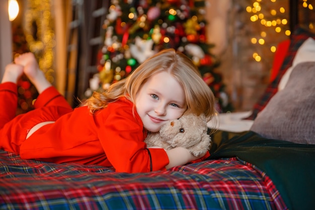 niña en pijama acostada en la cama abrazando a osito de peluche