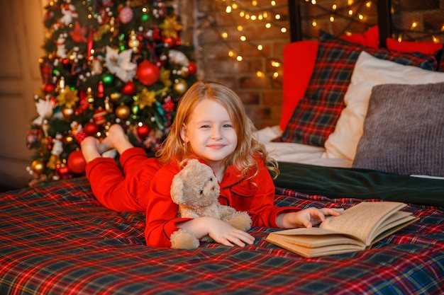 niña en pijama acostada en la cama abrazando a osito de peluche