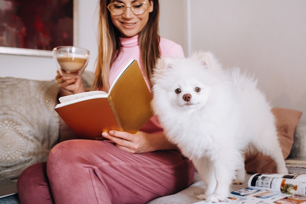 Una niña en pijama en casa lee un libro con su perro Spitzer, el perro y su dueño están descansando en el sofá y leyendo un libro. Tareas del hogar.