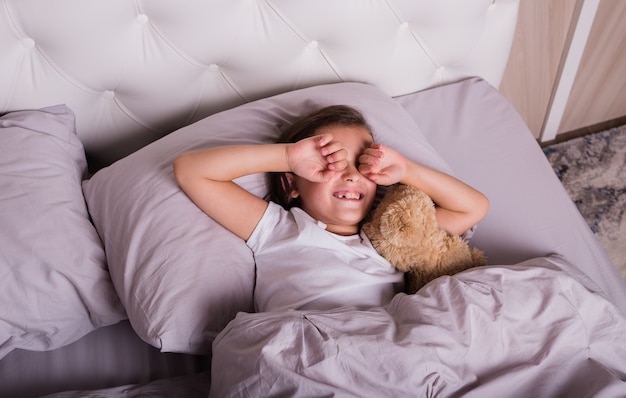 Foto una niña en pijama duerme en una cuna con un osito de peluche.