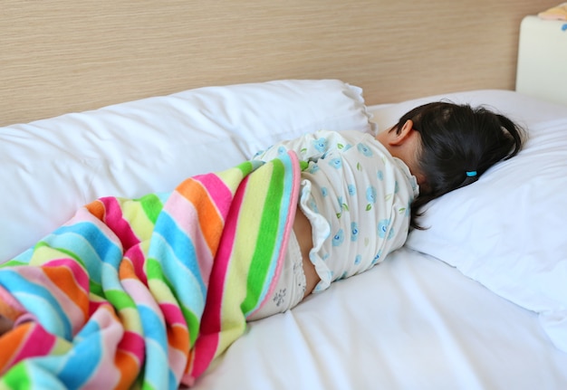 Niña en pijama durmiendo en la cama con manta