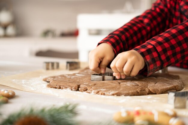 niña en pijama rojo cocinando pan de jengibre festivo en la cocina decorada con navidad. galletas de Navidad