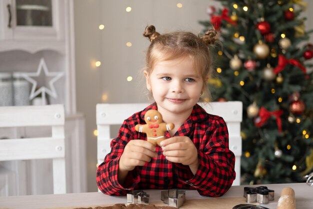 Niña en pijama rojo cocinar pan de jengibre festivo en cocina decorada de Navidad