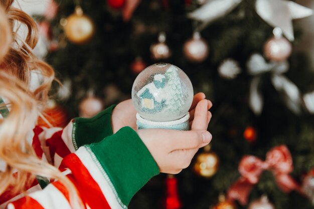 Foto una niña en pijama y un sombrero de navidad sostiene una bola de navidad: una bola de nieve. navidad