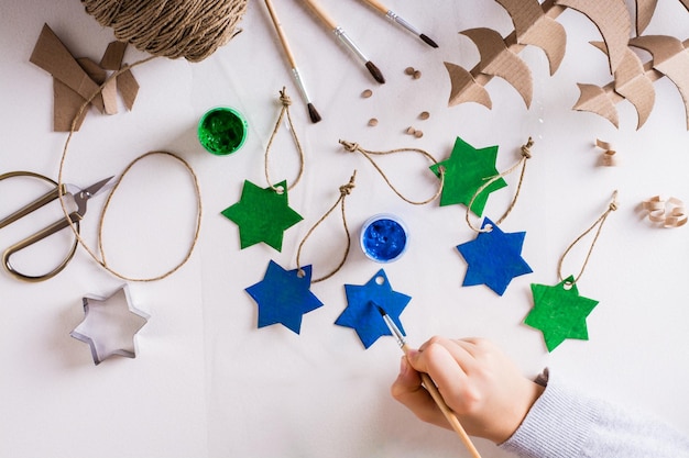 Una niña pinta una estrella de gouache de cartón para decoraciones navideñas hechas a mano de bricolaje Vista superior