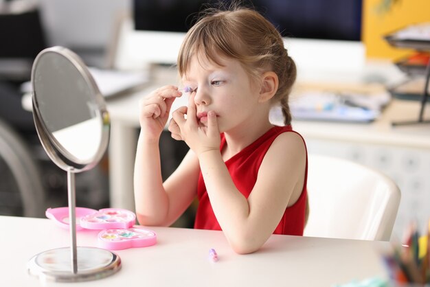 Niña se pinta los ojos y se mira en el espejo