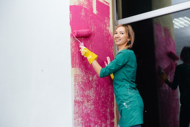 Una niña pinta una pared blanca en rosa con un primer plano de rodillo. Reparación del interior.