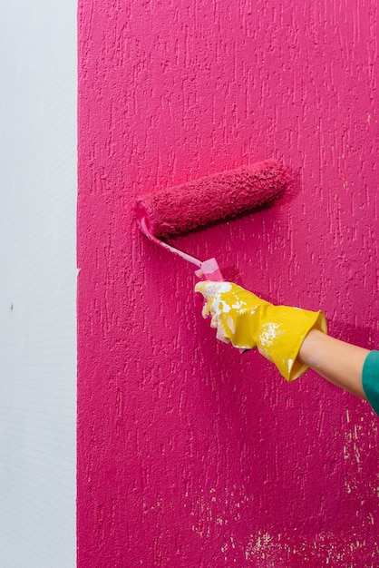 Una niña pinta una pared blanca en rosa con un primer plano de rodillo. Reparación del interior.