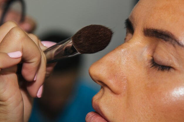 La niña pinta polvo en la cara, completa el maquillaje de ojos ahumados en el salón de belleza. Cuidado profesional de la piel.