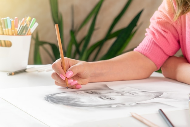 Una niña pinta un retrato de un hombre con un lápiz en un brillante estudio casero.