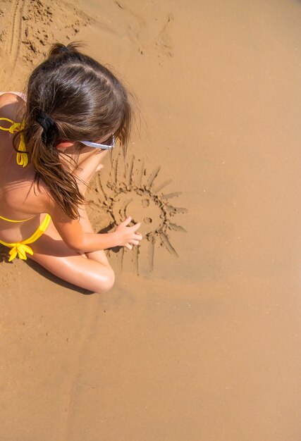 Niña pinta un sol en la arena