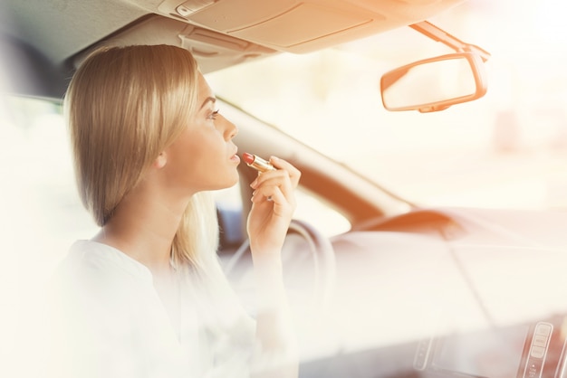 Niña pinta sus labios mientras está sentado al volante.