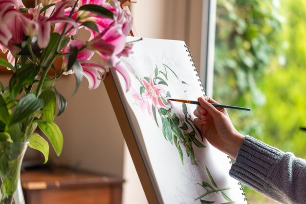 Niña pintando bodegones con flores lirios morados con pinturas de acuarela en el caballete