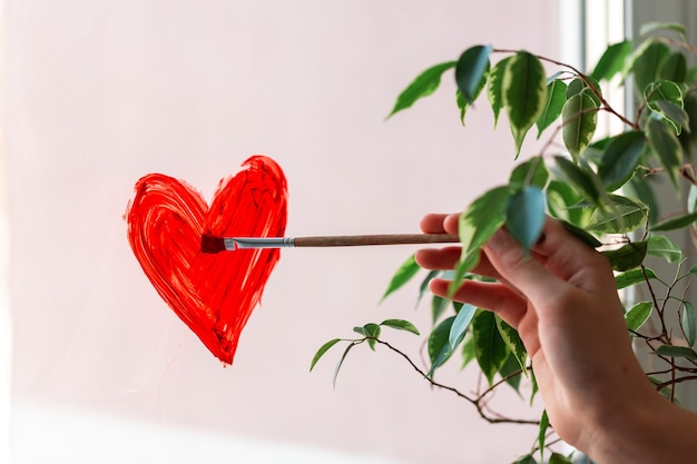 Niña pintando corazón rojo en la ventana