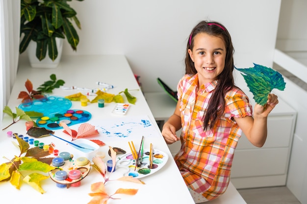 Niña pintando sobre hojas amarillas otoñales con gouache, artes infantiles, creatividad infantil, arte otoñal.