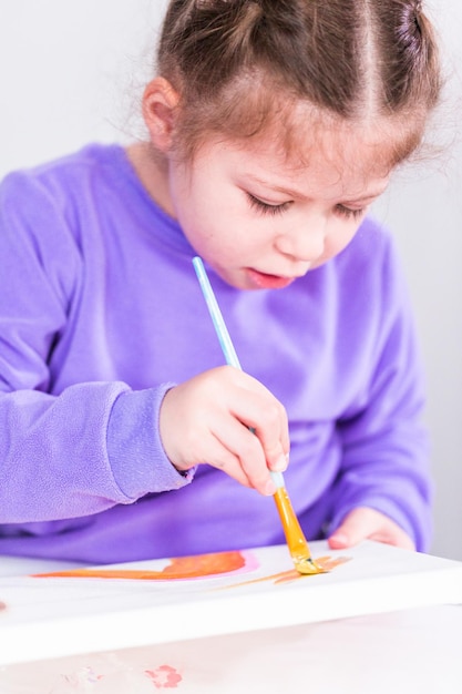 Niña pintando sobre lienzo con pintura acrílica.