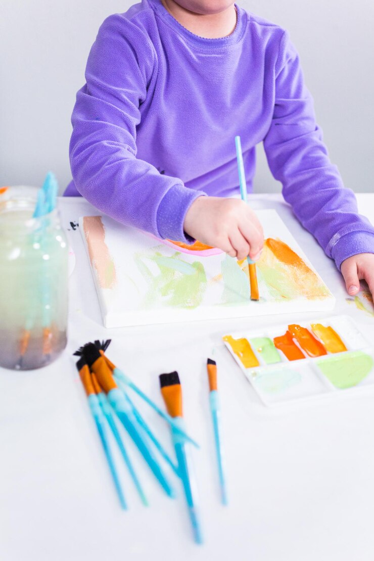 Foto niña pintando sobre lienzo con pintura acrílica.