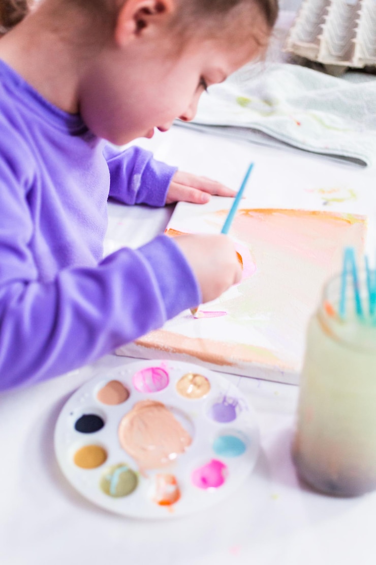 Foto niña pintando sobre lienzo con pintura acrílica.