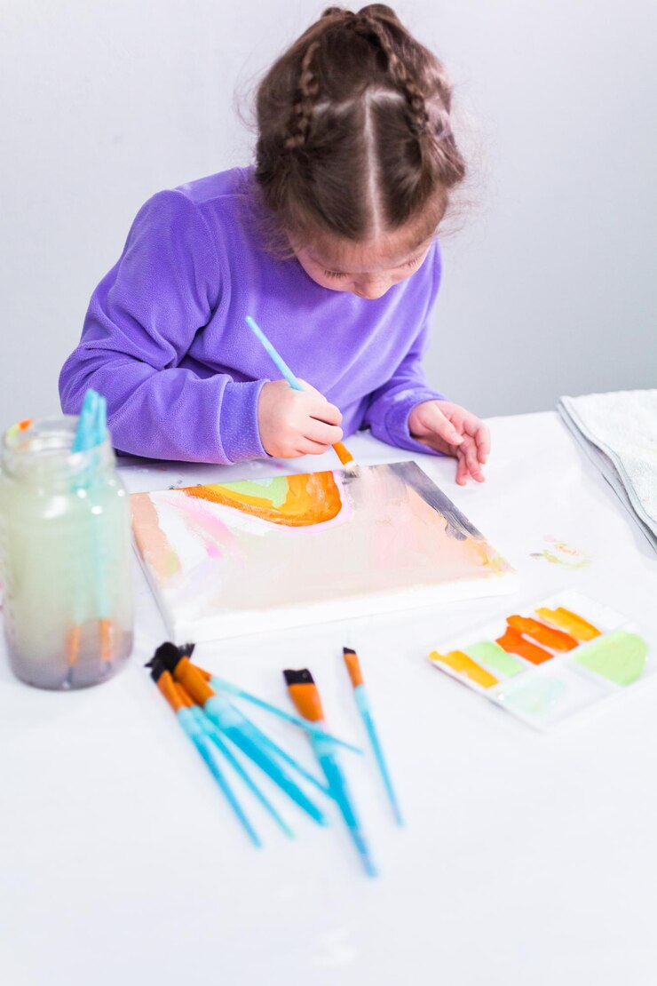 Foto niña pintando sobre lienzo con pintura acrílica.
