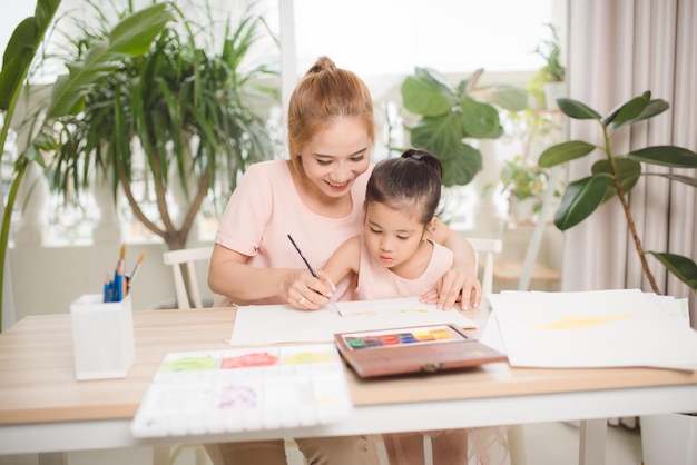 Niña pintando con su madre recostada en el salón