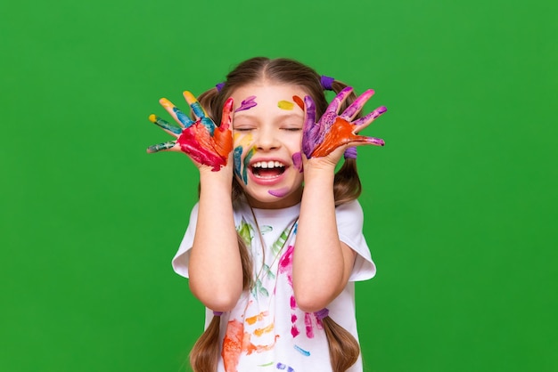 Una niña con pintura, un niño se ha manchado las manos y la cara con pintura y está feliz Una niña con las manos manchadas con pintura en un fondo aislado