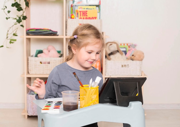 Niña con pintura portátil en la educación escolar en casa Dibujo de niños en edad preescolar usando lecciones en línea